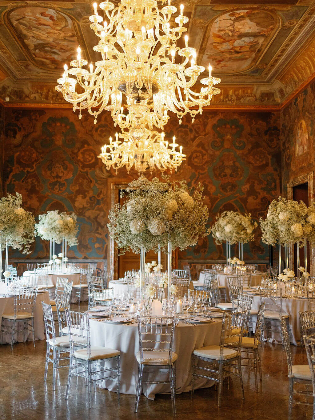 eingedeckte runde Tische im Hochzeitssaal mit großen Blumeninstallationen