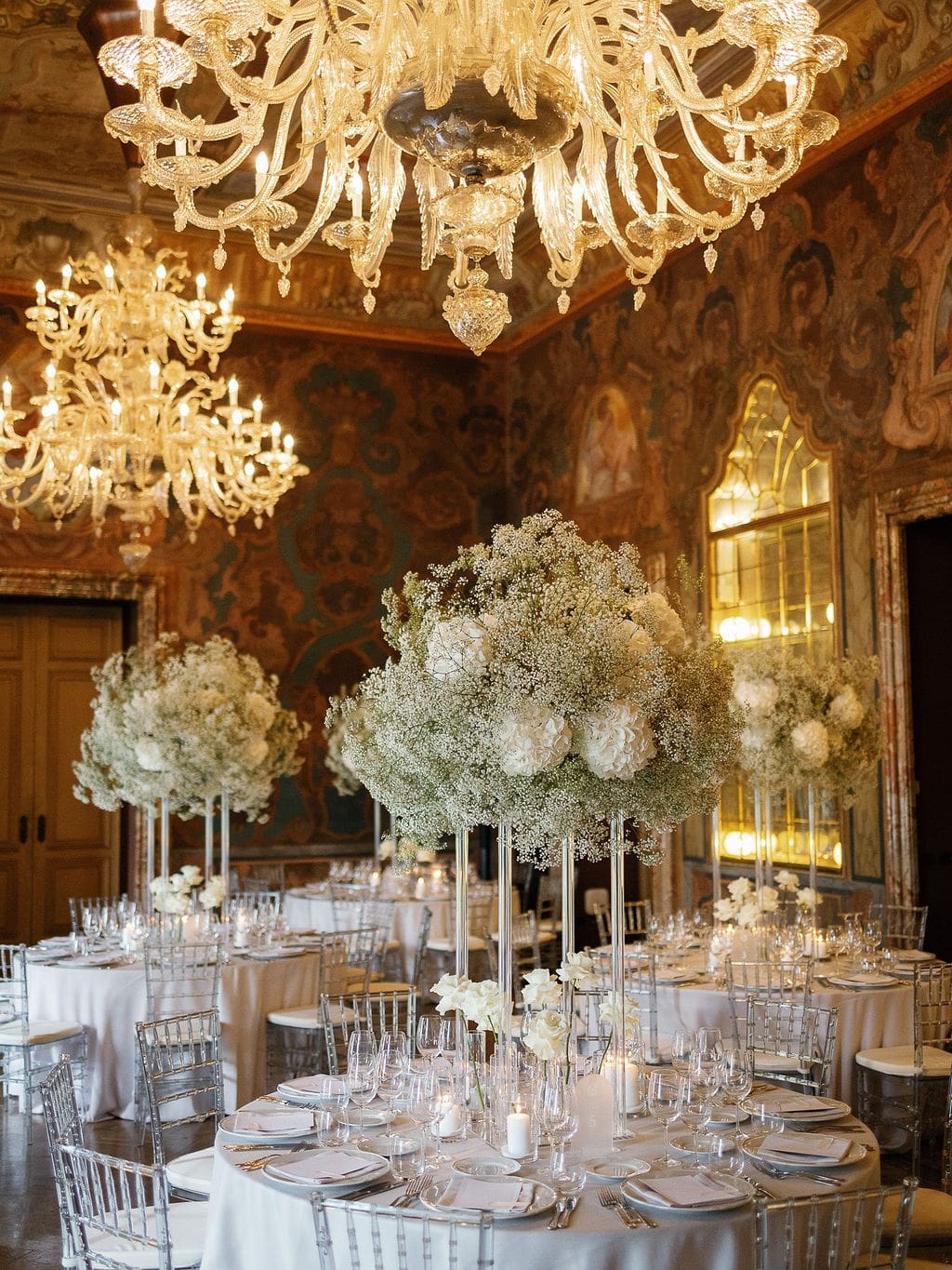 Festlich dekorierter Ballsaal mit opulenten Kronleuchtern und Blumenarrangements in Weiß und Creme.