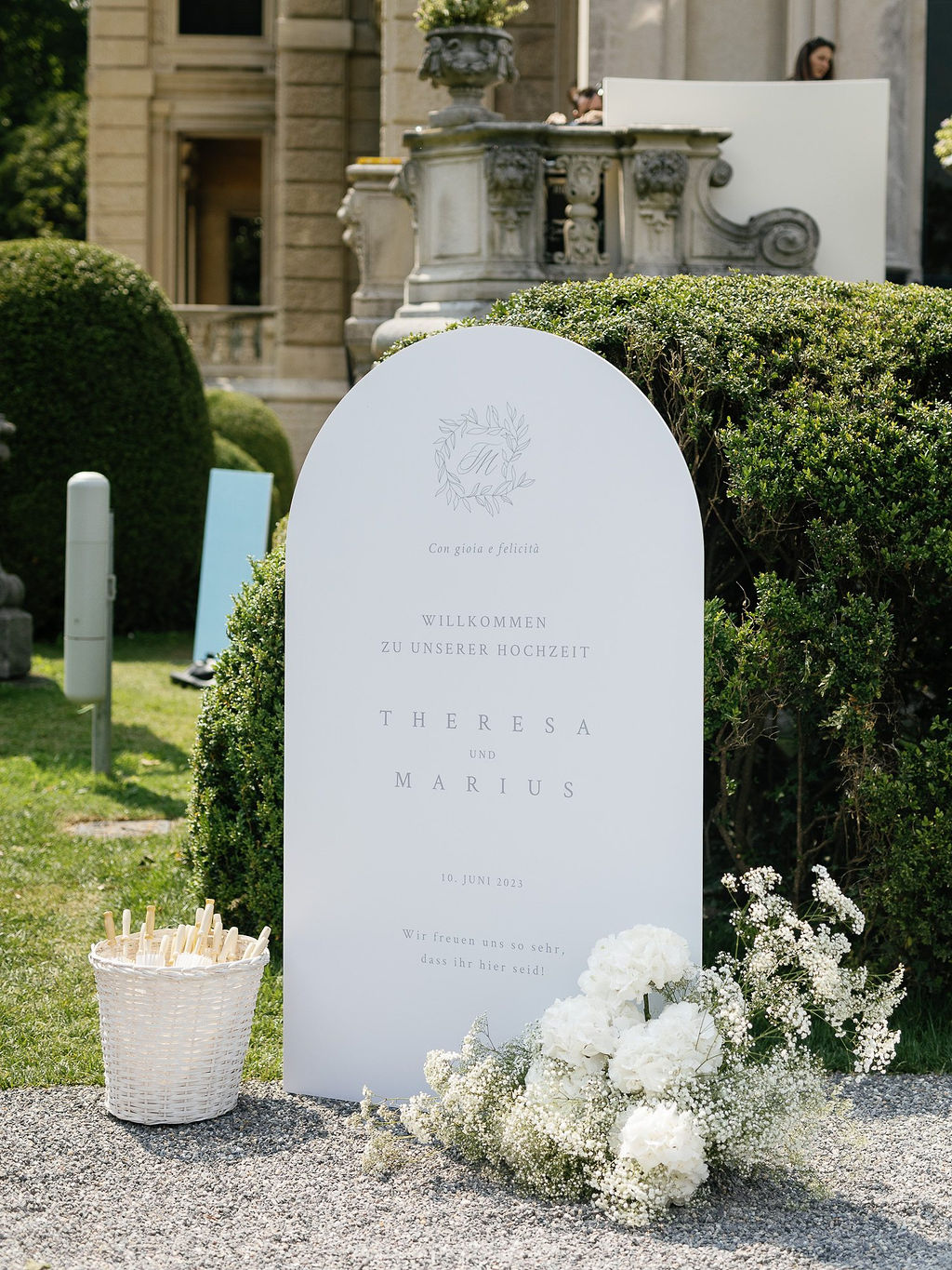 Willkommensschild mit floralen Akzenten und der Aufschrift "Theresa und Marius – Hochzeit am Comer See".