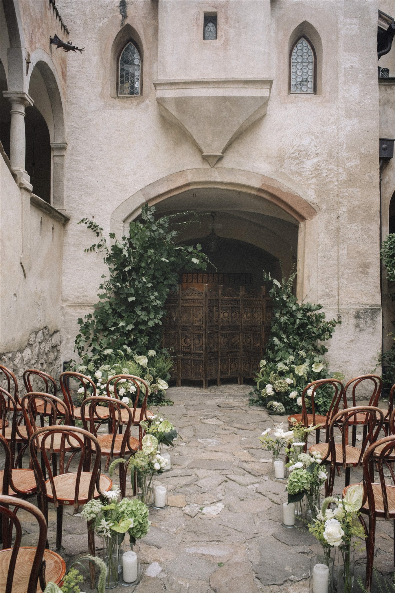 Romantische Zeremonie in einem historischen Innenhof, dekoriert mit grünen Pflanzen und weißen Blumen.