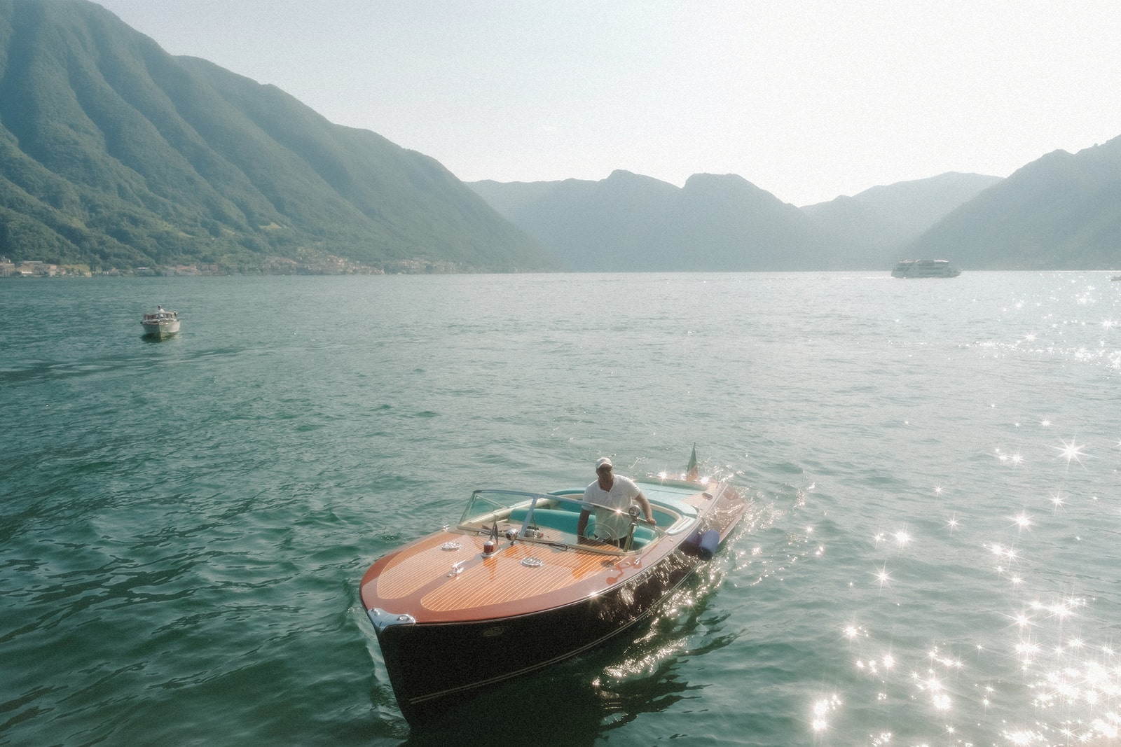 Holzboot auf dem ruhigen Lake Como mit sonnigen Reflexionen und grüner Bergkulisse.