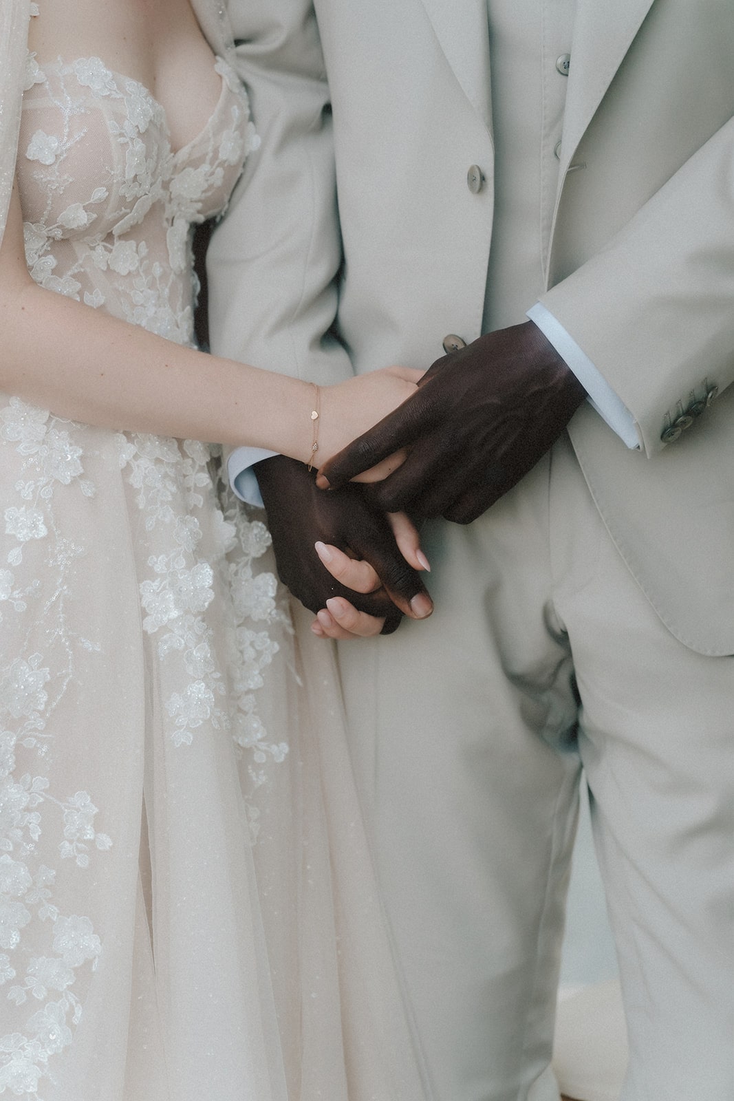 Detailaufnahme der ineinander verschlungenen Hände eines Hochzeitspaares mit eleganter Garderobe.