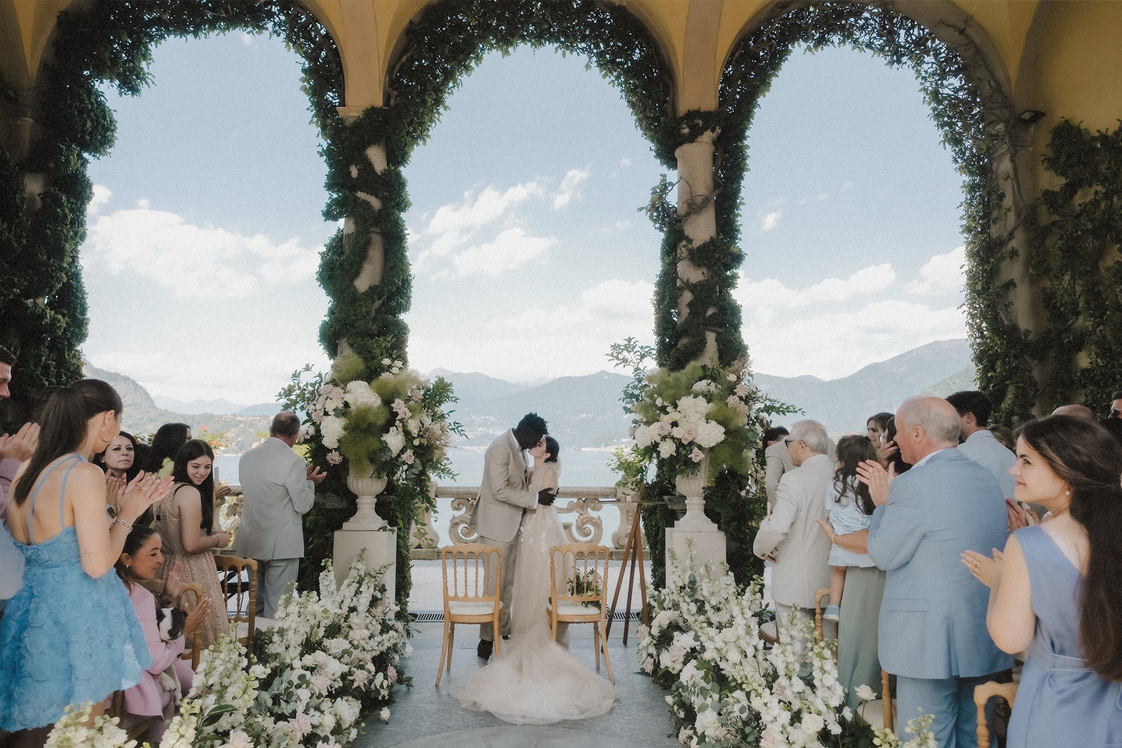 Das Brautpaar küsst sich vor einer Kulisse aus Blumen und dem atemberaubenden Lake Como.