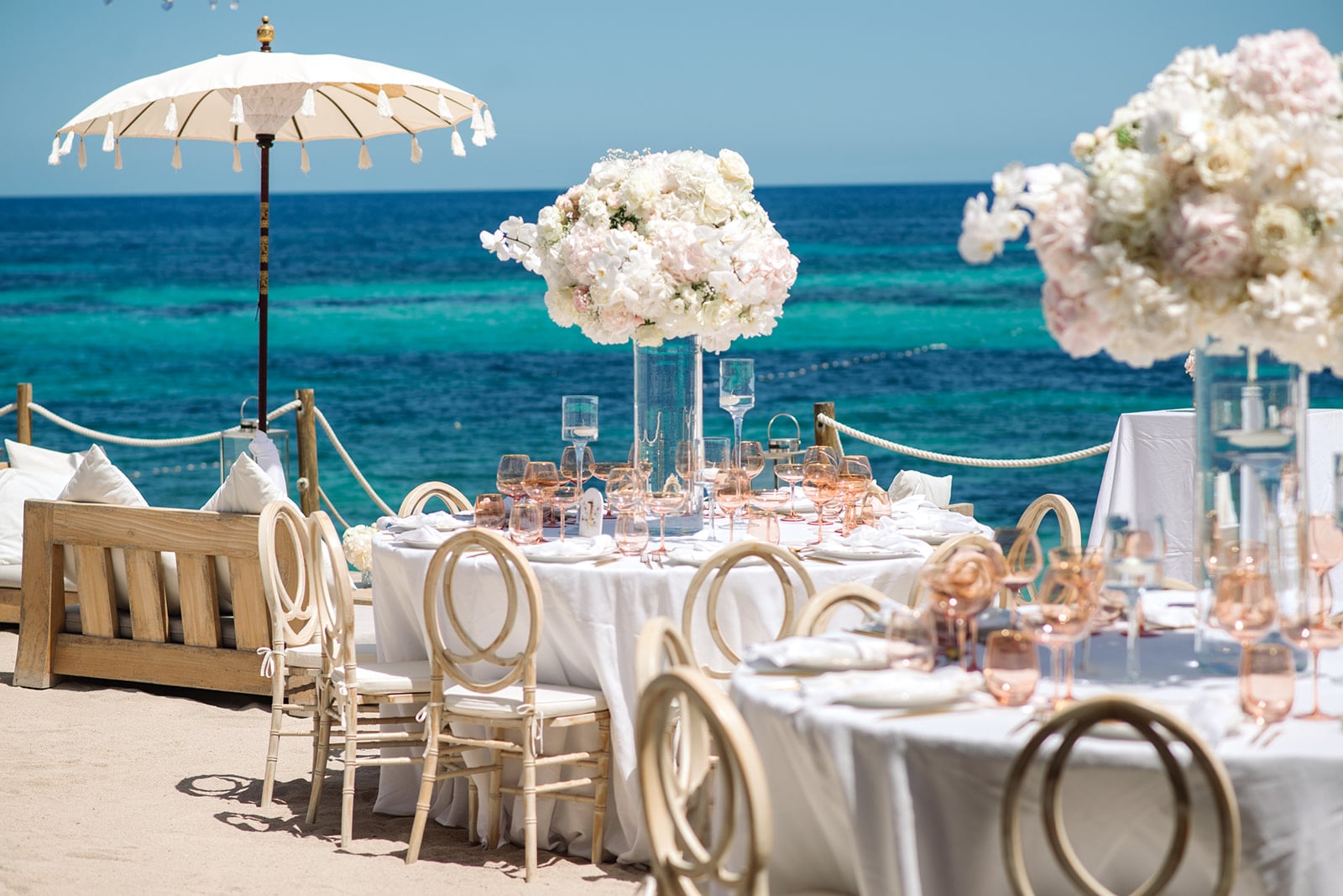 Elegante Hochzeitstafel am Strand in Ibiza mit luxuriösen Blumengestecken und Kerzen, die eine romantische Atmosphäre schaffen