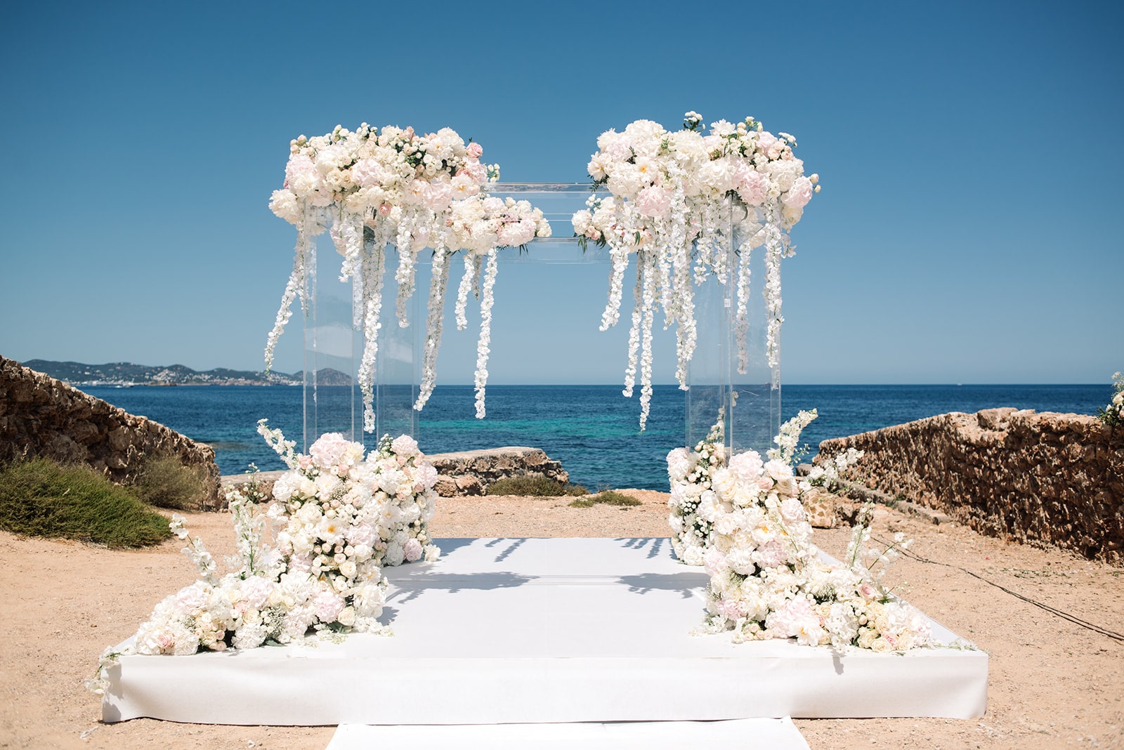 Atemberaubender Traubogen aus weißen und rosafarbenen Blumen vor der Kulisse des Ozeans auf Ibiza.