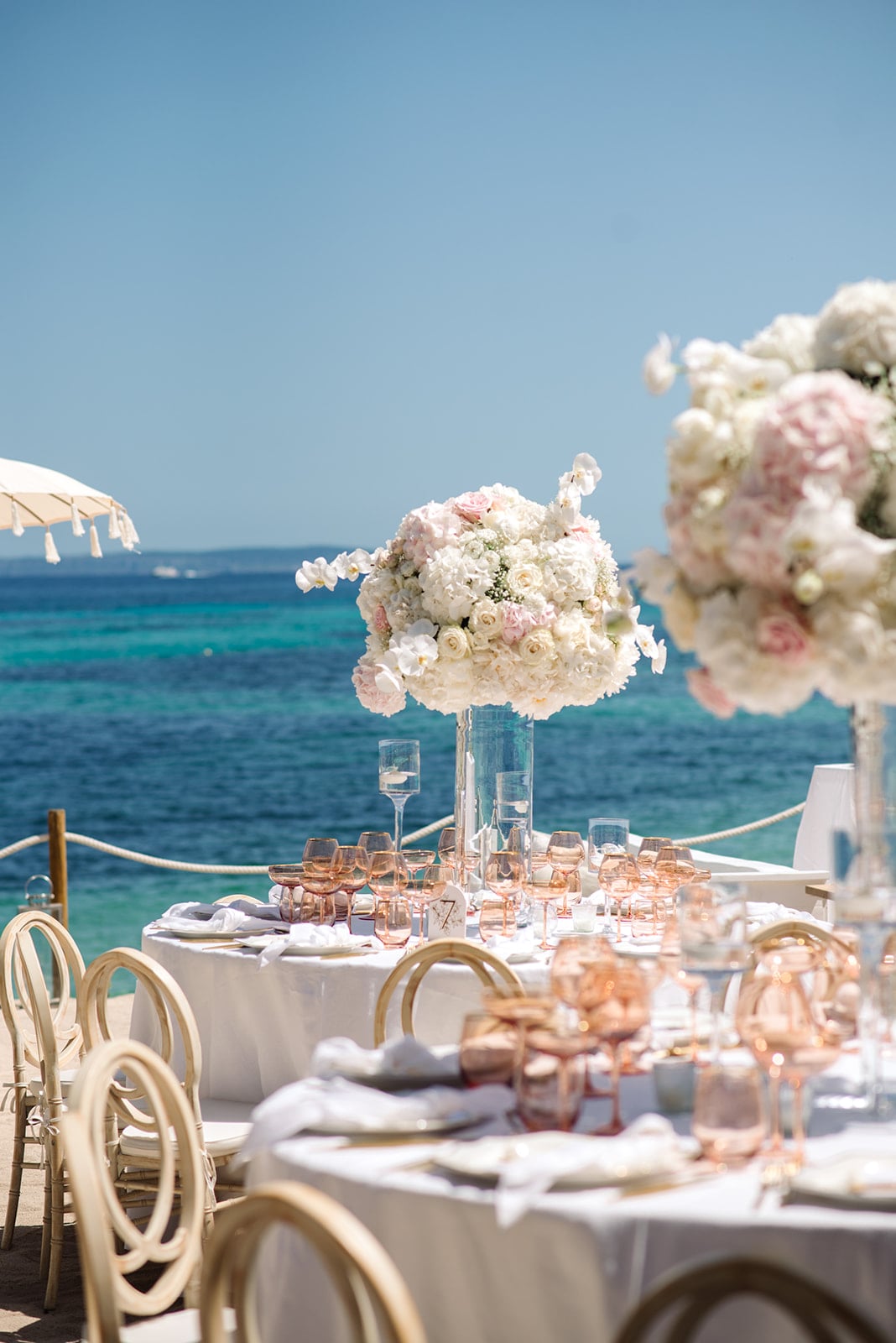 Hochzeitstafel am Strand mit opulenten Blumengestecken und exklusiver Dekoration unter strahlendem Himmel.