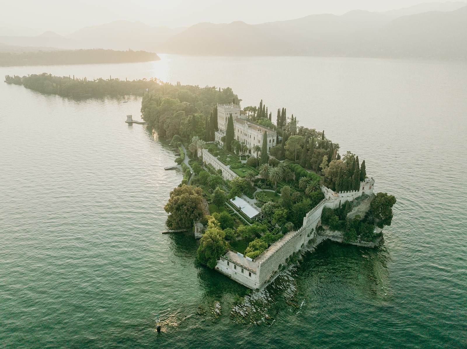 Sonnenuntergangsaufnahme einer idyllischen Insel mit einer luxuriösen Villa, mediterranen Gärten und einer zauberhaften Atmosphäre.