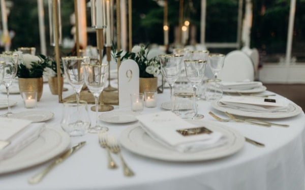 Festlich gedeckter Hochzeitstisch in Weiß und Gold, verziert mit Kerzen, Blumenarrangements und stilvollen Gläsern für eine elegante Abendfeier.