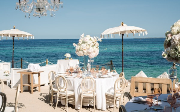 Luxuriöse Strandhochzeit mit Kronleuchter, eleganten Tischen und einem klaren blauen Himmel.