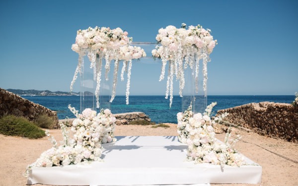 Atemberaubender Traubogen aus weißen und rosafarbenen Blumen vor der Kulisse des Ozeans auf Ibiza.