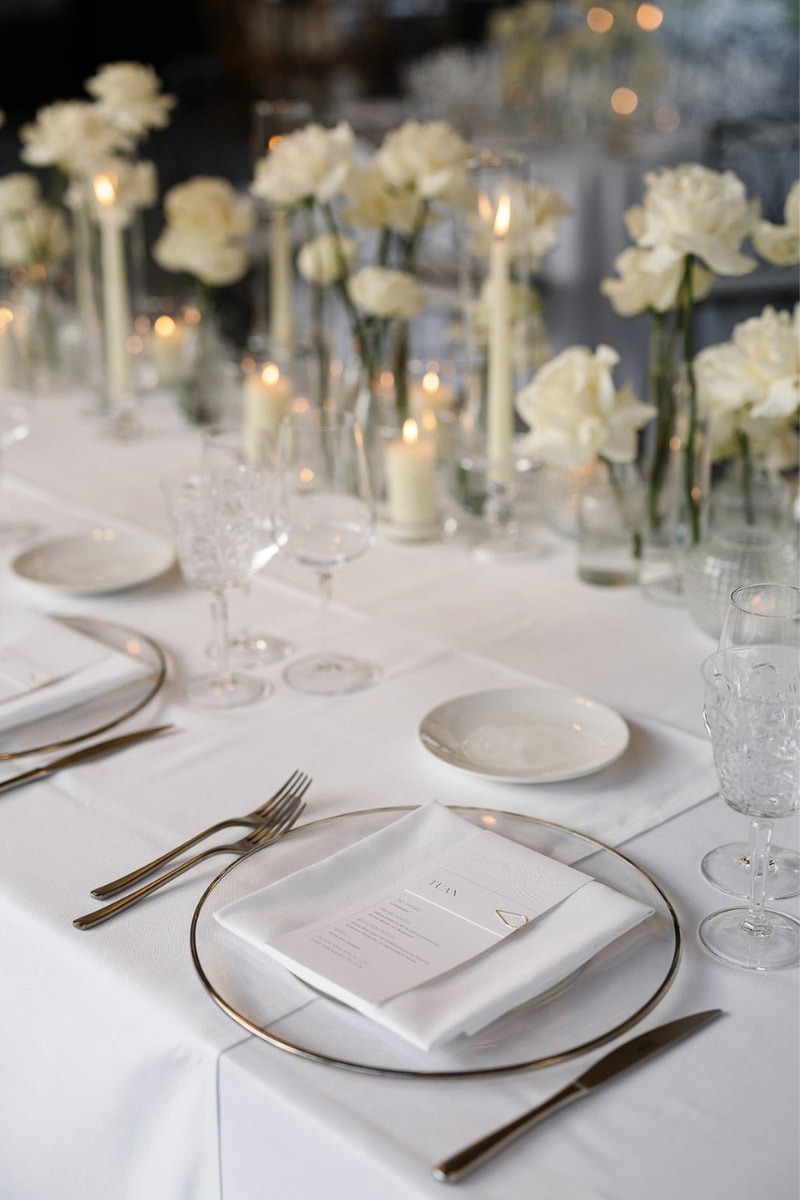 Großes Elegante Hochzeitstafel mit weißen Rosen, Kerzen und gläsernen Details, die für ein romantisches Ambiente sorgen.