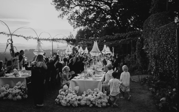 Gäste stoßen bei einer eleganten Outdoor-Hochzeit im Garten unter funkelnden Lichtern an.